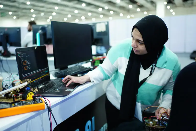 Participant coding on a laptop next to a robot kit, Connecta 2025