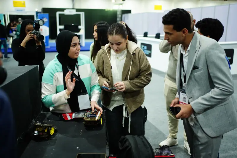 Participants gather excitedly around a robot car they are building, Connecta 2025