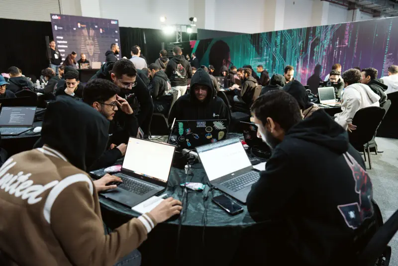 CTF teams hunched over laptops under the neon cyber backdrop, Connecta 2025