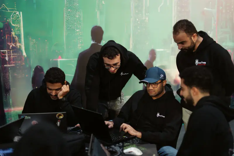 Team members huddle around one laptop to crack a challenge, Connecta 2025