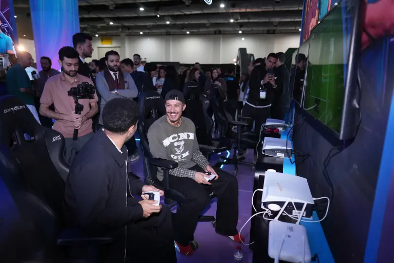 Guests laugh during a PS5 football match as a crowd watches, Connecta 2025