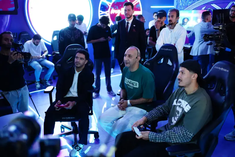 Guests play PS5 in a neon-blue gaming lounge surrounded by onlookers, Connecta 2025